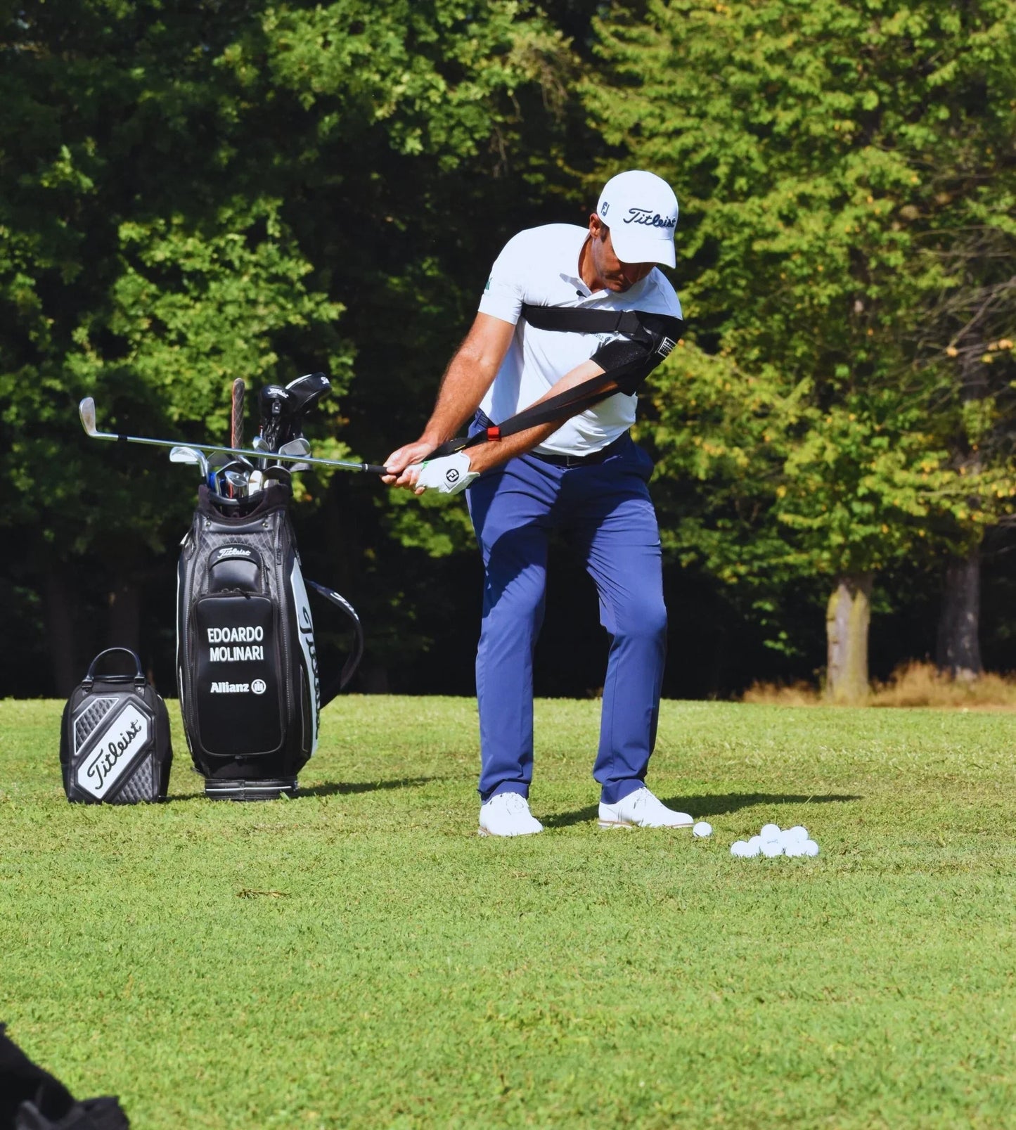 Golfer wearing Tour Feel swing trainer device practicing golf swing with clubs and ball on grass field